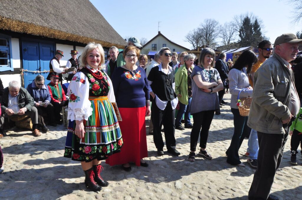 Goście wydarzenia i osoby w strojach regionalnych gromadzą się na brukowanym dziedzińcu Zagrody Jamneńskiej w słoneczny dzień (kliknięcie powiększy zdjęcie).