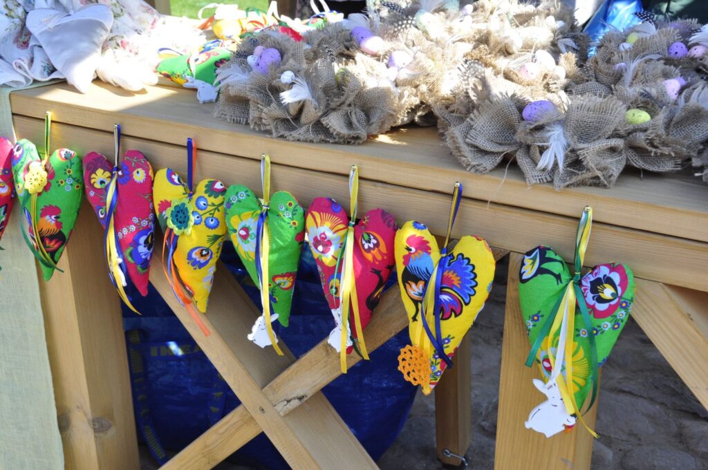 Rząd kolorowych, ręcznie szytych serc z materiału w ludowe wzory, zawieszonych na sznurkach przy drewnianym stole (kliknięcie powiększy zdjęcie).