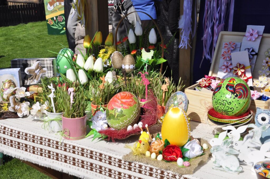 Zbliżenie na wielkanocne dekoracje: bogato zdobione pisanki, bazie oraz wiosenne kwiaty ułożone w koszyczkach na białym obrusie (kliknięcie powiększy zdjęcie).