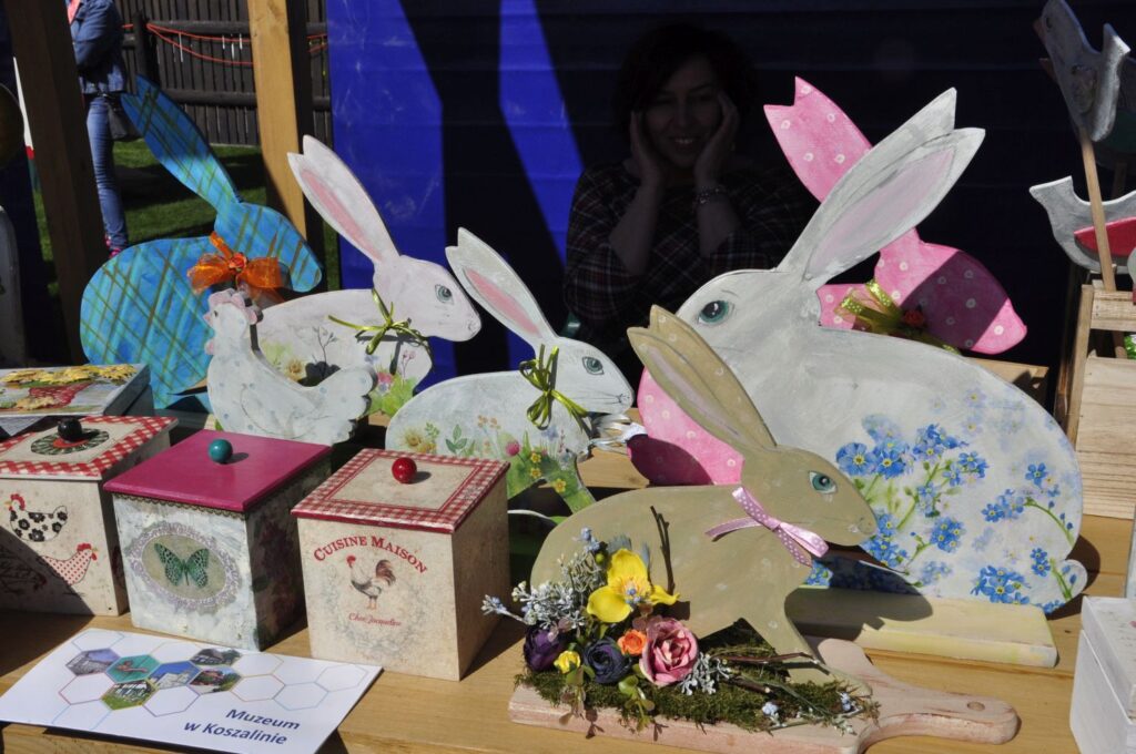 Stoisko z wielkanocnymi ozdobami, na którym stoją drewniane, malowane zajączki oraz ozdobne puszki z motywami kwiatowymi (kliknięcie powiększy zdjęcie).