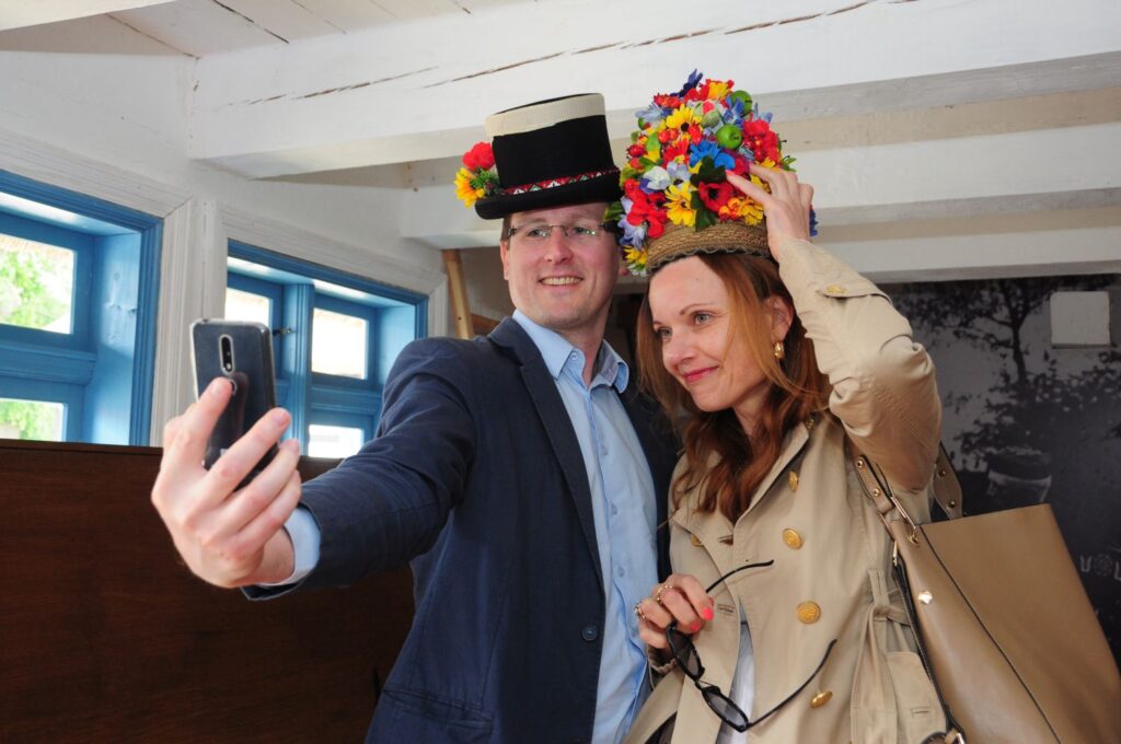 Para zwiedzających robi sobie pamiątkowe zdjęcie w muzealnym wnętrzu, przymierzając tradycyjne, jamneńskie nakrycia głowy (kliknięcie powiększy zdjęcie).