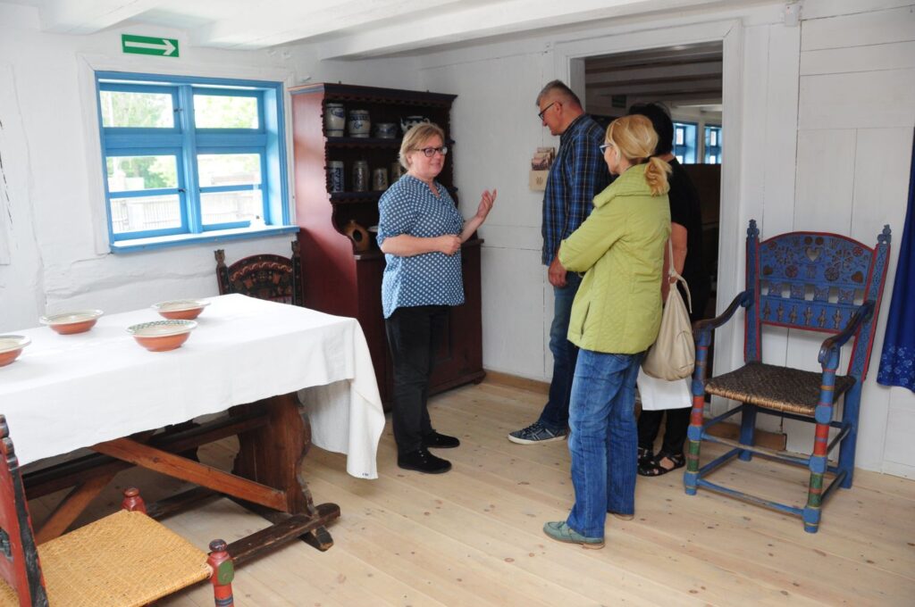 Grupa dorosłych zwiedzających rozmawia z przewodnikiem na wystawie kultury jamneńskiej (kliknięcie powiększy zdjęcie).