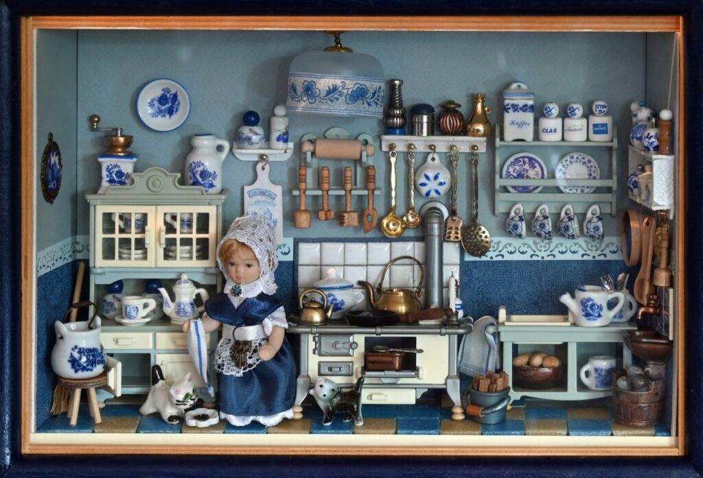 Miniaturowe wnętrze przedstawiające kuchnię z licznymi naczyniami, półkami, piecem i lalką w stroju ludowym (kliknięcie powiększy zdjęcie).