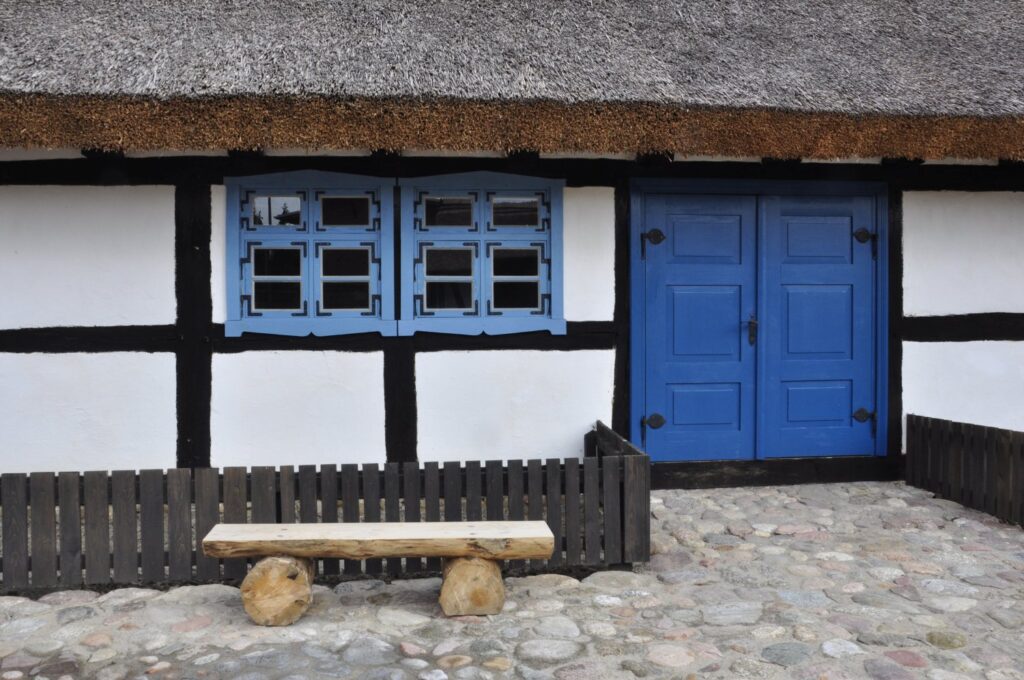 Zbliżenie na fasadę tradycyjnej chaty z niebieskimi drzwiami i oknami oraz drewnianą ławką ustawioną przed wejściem (kliknięcie powiększy zdjęcie).