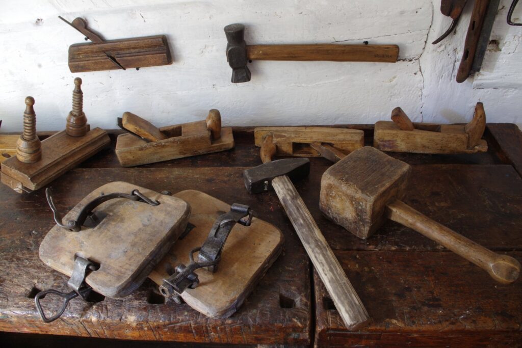 Zestaw dawnych narzędzi stolarskich i ciesielskich ułożonych na drewnianym blacie roboczym w warsztacie (kliknięcie powiększy zdjęcie).