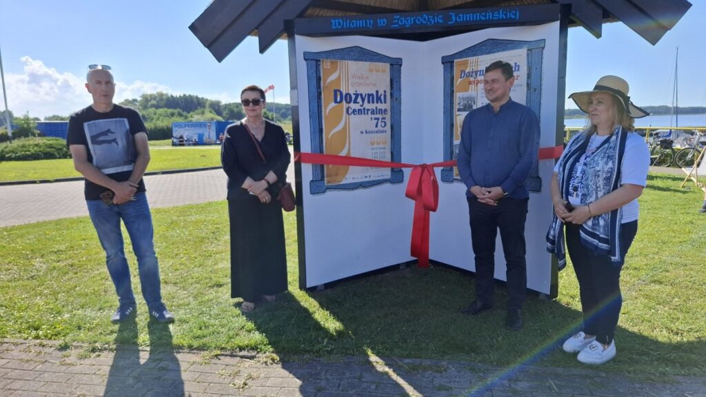 Uczestnicy stojący przy Witaczu Jamneńskim, na którym zawieszone są plakaty o wydarzeniach (kliknięcie powiększy zdjęcie)