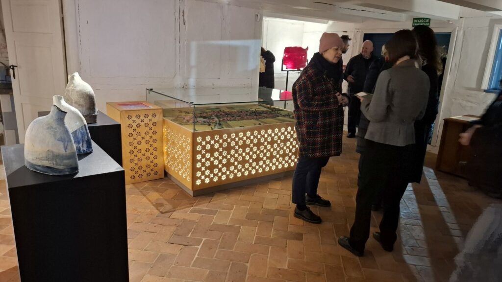 Zwiedzający oglądający prace artystyczne rozmieszczone na postumentach i w gablotach muzealnych (kliknięcie powiększy zdjęcie)