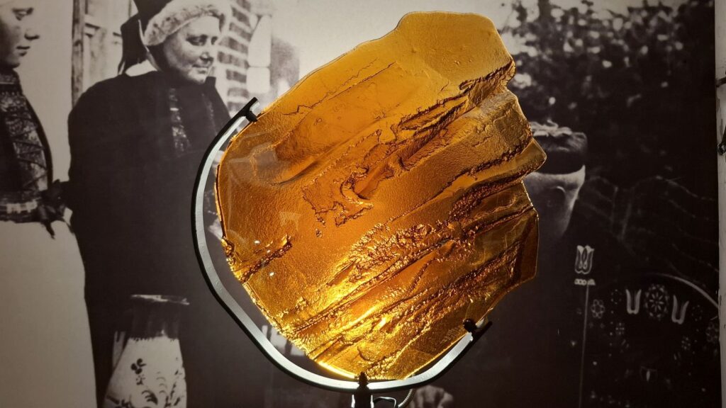 Detal pracy artystycznej – okrągły obiekt z bursztynową, fakturowaną powierzchnią na tle archiwalnej fotografii (kliknięcie powiększy zdjęcie)