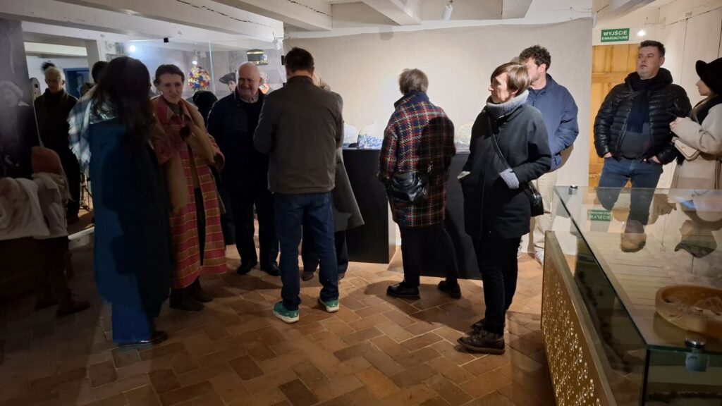 Grupa odwiedzających rozmawiających w sali wystawowej podczas wernisażu (kliknięcie powiększy zdjęcie)