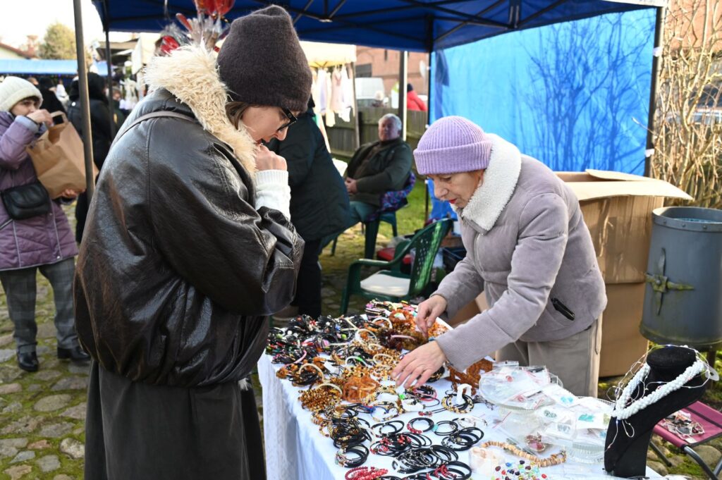 Uczestniczki jarmarku przeglądają i wybierają biżuterię oraz drobne rękodzieło na stoisku pod namiotem (kliknięcie powiększy zdjęcie).